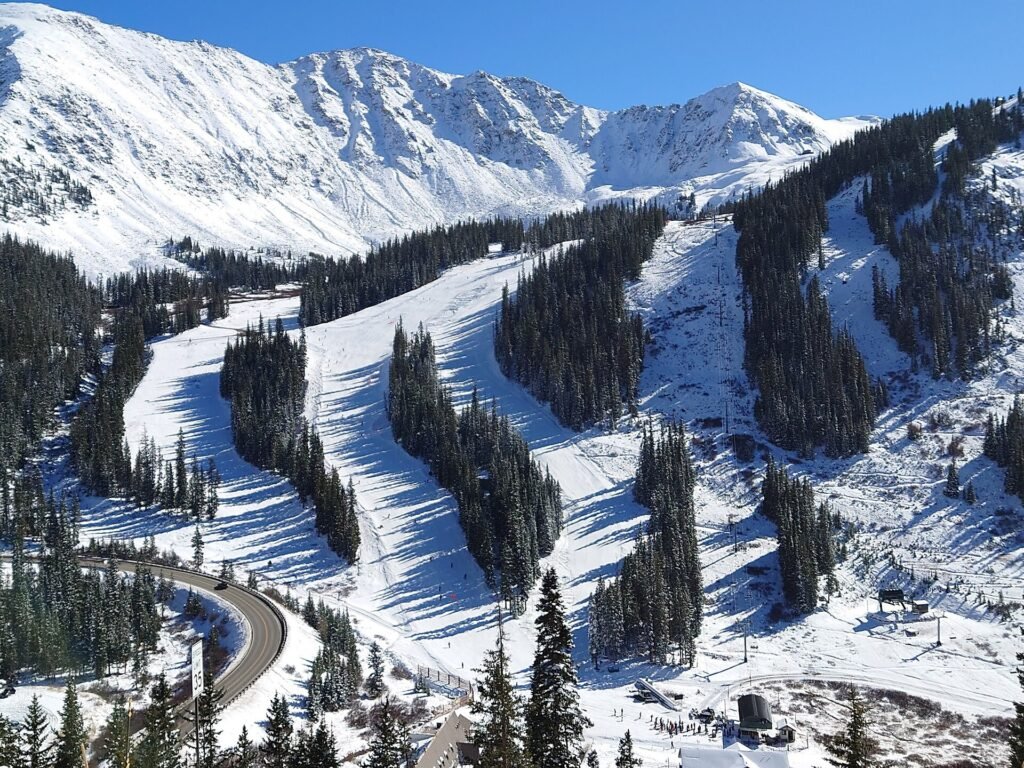 Colorado'daki Arapahoe Basin kayak merkezinde karla kaplı alt pistler, ağaçlar arasındaki parkurlar ve arkada karlı zirveler