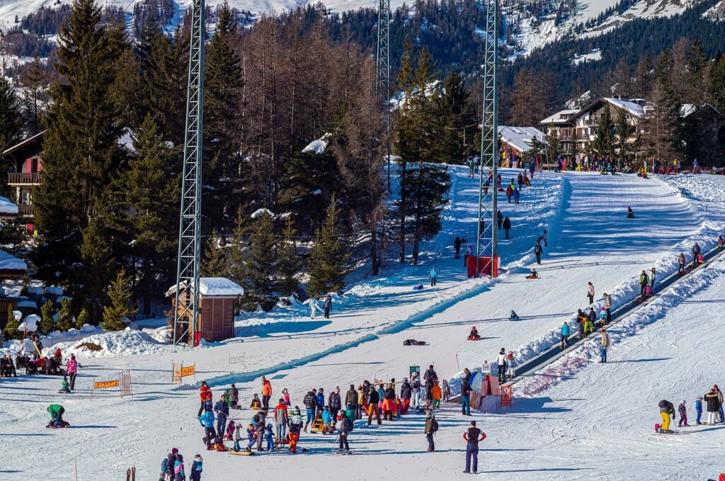 Crans-Montana'da güneşli bir kış gününde başlangıç pisti, yürüyen bant ve kızak kayan çocuklar