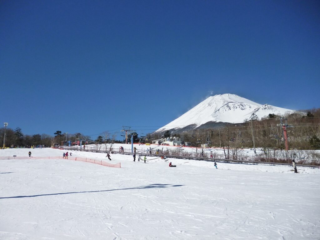 Fuji Dağı eteklerindeki Snow Park Yeti kayak merkezinde karla kaplı pist, telesiyejler ve arkada karlı Fuji zirvesi