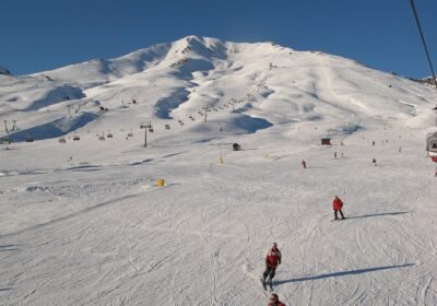 Passo del Tonale'de güneşli bir günde geniş pistte kayak yapanlar ve arkada telesiyejlerin çıktığı karlı dağ